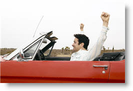 Man in classic red convertible with both arms raised high with delight